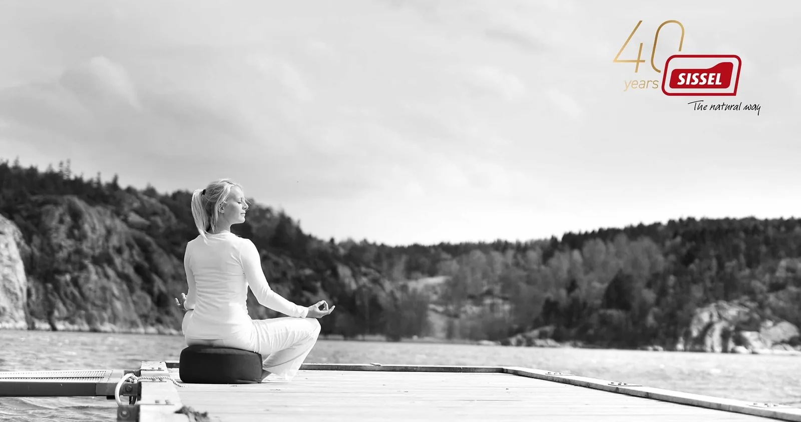 黑白照片：一位女士盘腿坐在瑞典湖畔的栈桥上，附 SISSEL 40 周年标记